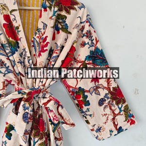 May include: A white cotton robe with a floral print in shades of red, blue, and green. The robe has a tie belt and a yellow and white striped lining. The text "Indian Patchworks" is visible on the robe.