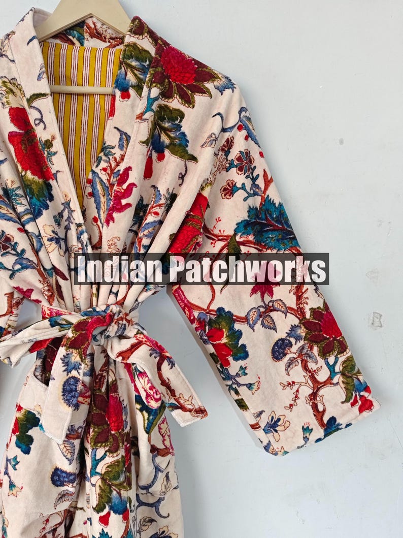 May include: A white cotton robe with a floral print in shades of red, blue, and green. The robe has a tie belt and a yellow and white striped lining. The text "Indian Patchworks" is visible on the robe.