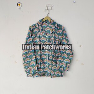 May include: A long-sleeved pajama top with a floral pattern in teal, pink, and blue, with white trim. The shirt is button-down and hangs on a wooden hanger. The text "Indian Patchworks" is across the front.