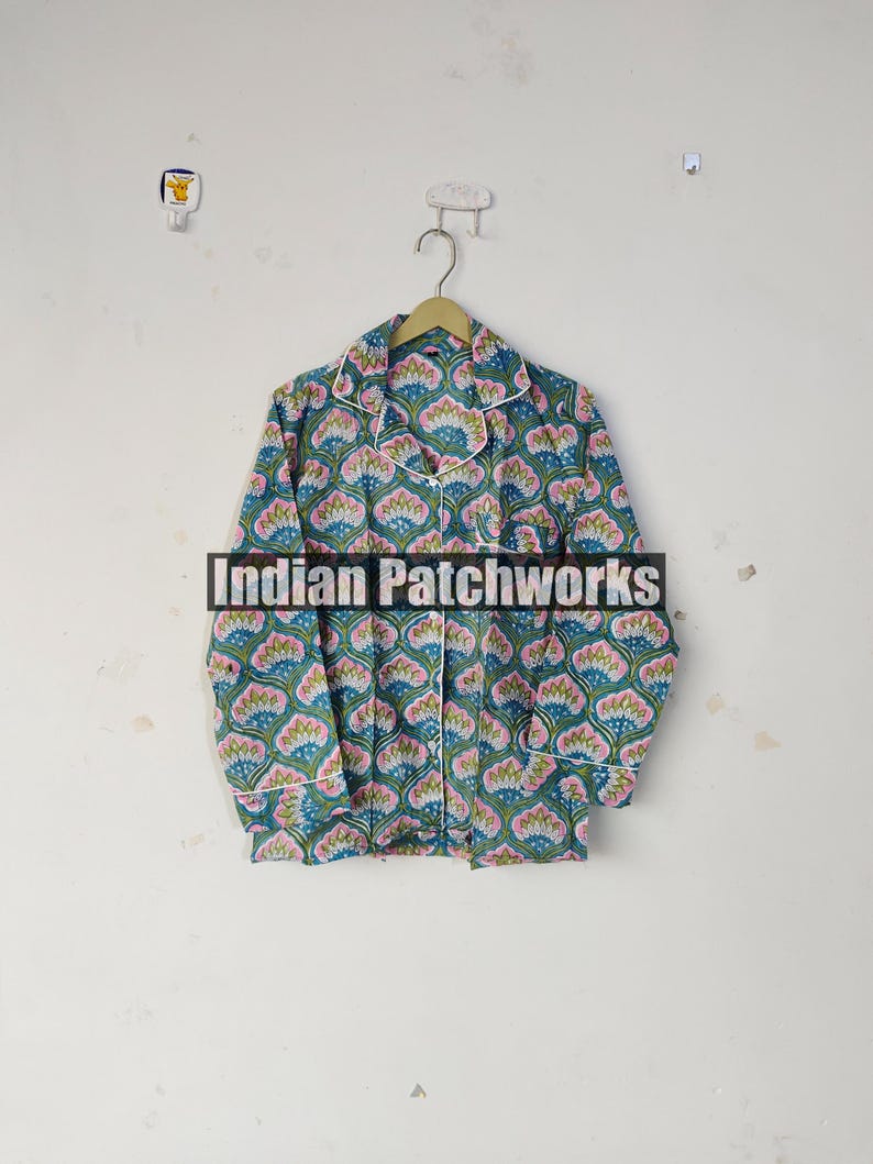 May include: A long-sleeved pajama top with a floral pattern in teal, pink, and blue, with white trim. The shirt is button-down and hangs on a wooden hanger. The text "Indian Patchworks" is across the front.