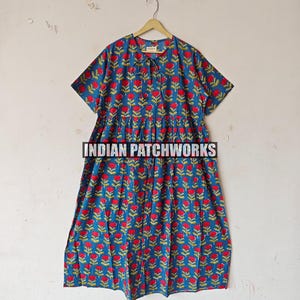 Puede incluir: Vestido azul con estampado floral rojo y mangas cortas, colgado de una percha de madera. El texto "INDIAN PATCHWORKS" es visible en el vestido.