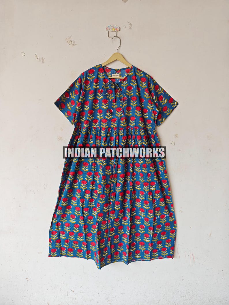 May include: A blue dress with a red floral pattern and short sleeves, hanging on a wooden hanger. The text "INDIAN PATCHWORKS" is visible on the dress.