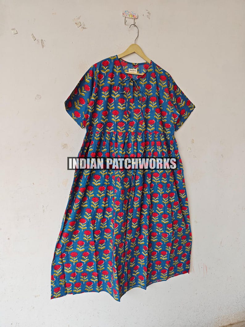 May include: A blue dress featuring a red floral design. The dress has short sleeves and a gathered waist. The text "INDIAN PATCHWORKS" is visible at the bottom of the image.