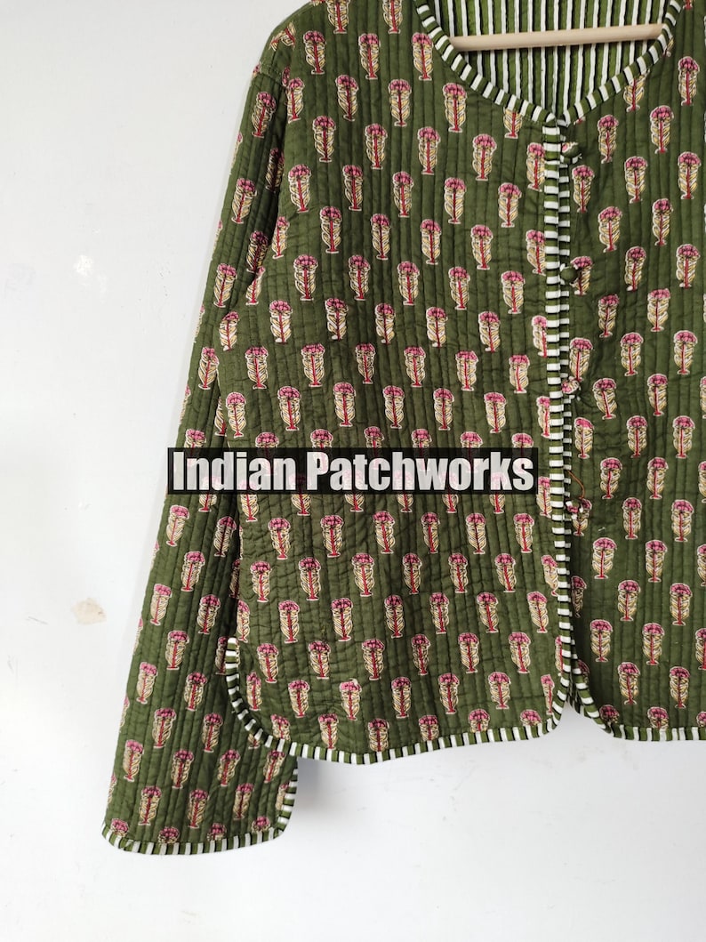 May include: Olive green quilted jacket with a repeating pink floral pattern. The jacket has a white and black striped trim and the text "Indian Patchworks". The jacket is buttoned up and has long sleeves.
