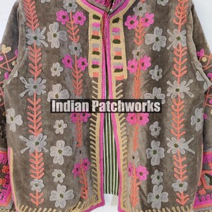 May include: A brown jacket with pink, grey, and peach floral embroidery. The jacket has a high collar and a striped lining. The text "Indian Patchworks" is visible on the front.