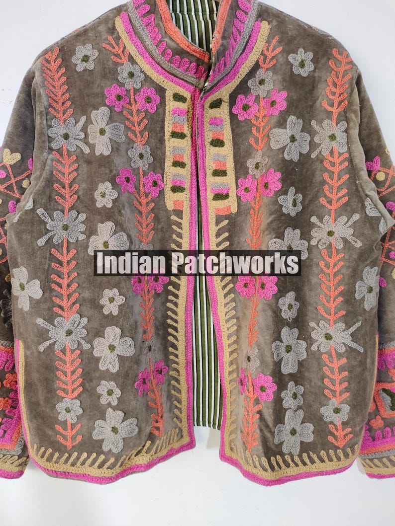 May include: A brown jacket with pink, grey, and peach floral embroidery. The jacket has a high collar and a striped lining. The text "Indian Patchworks" is visible on the front.
