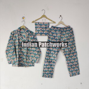 May include: A three-piece pajama set featuring a button-down shirt, pants, and a matching eye mask. The set is adorned with a repeating floral pattern in shades of teal, pink, and white. The text "Indian Patchworks" is visible.