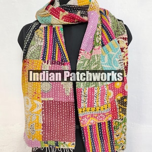 Puede incluir: Una bufanda de patchwork colorida con el texto "Indian Patchworks" se muestra en un maniqu&iacute;. La bufanda presenta una variedad de telas en tonos de amarillo, rosa, morado y azul, cosidas con hilo blanco. La bufanda tiene un borde con flecos.