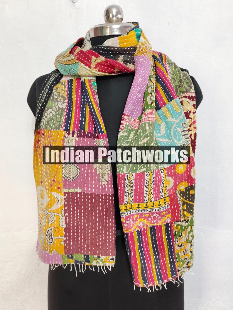 Puede incluir: Una bufanda de patchwork colorida con el texto "Indian Patchworks" se muestra en un maniqu&iacute;. La bufanda presenta una variedad de telas en tonos de amarillo, rosa, morado y azul, cosidas con hilo blanco. La bufanda tiene un borde con flecos.