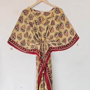 May include: A beige kaftan with a red and black floral print. The kaftan has a V-neck and short sleeves. It is tied at the waist with a red cord.