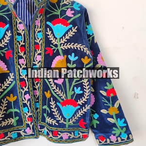 May include: A navy blue velvet jacket with colorful floral embroidery. The jacket has a mandarin collar and long sleeves. The embroidery is intricate and detailed, featuring a variety of flowers and leaves. The jacket is a unique and stylish piece of clothing.