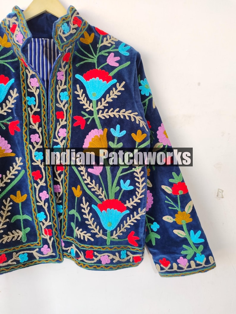 May include: A navy blue velvet jacket with colorful floral embroidery. The jacket has a mandarin collar and long sleeves. The embroidery is intricate and detailed, featuring a variety of flowers and leaves. The jacket is a unique and stylish piece of clothing.