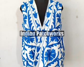 May include: A white sleeveless vest with a deep V-neckline and blue floral embroidery. The vest is on a mannequin. The text "Indian Patchworks" is visible on the vest.