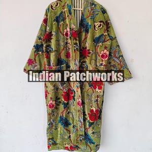 May include: A green velvet robe with a floral print. The robe has a long, flowing silhouette and a wide collar. The robe is open at the front, revealing a white and green striped lining. The robe has two pockets on the front. The text "Indian Patchworks" is visible on the robe.
