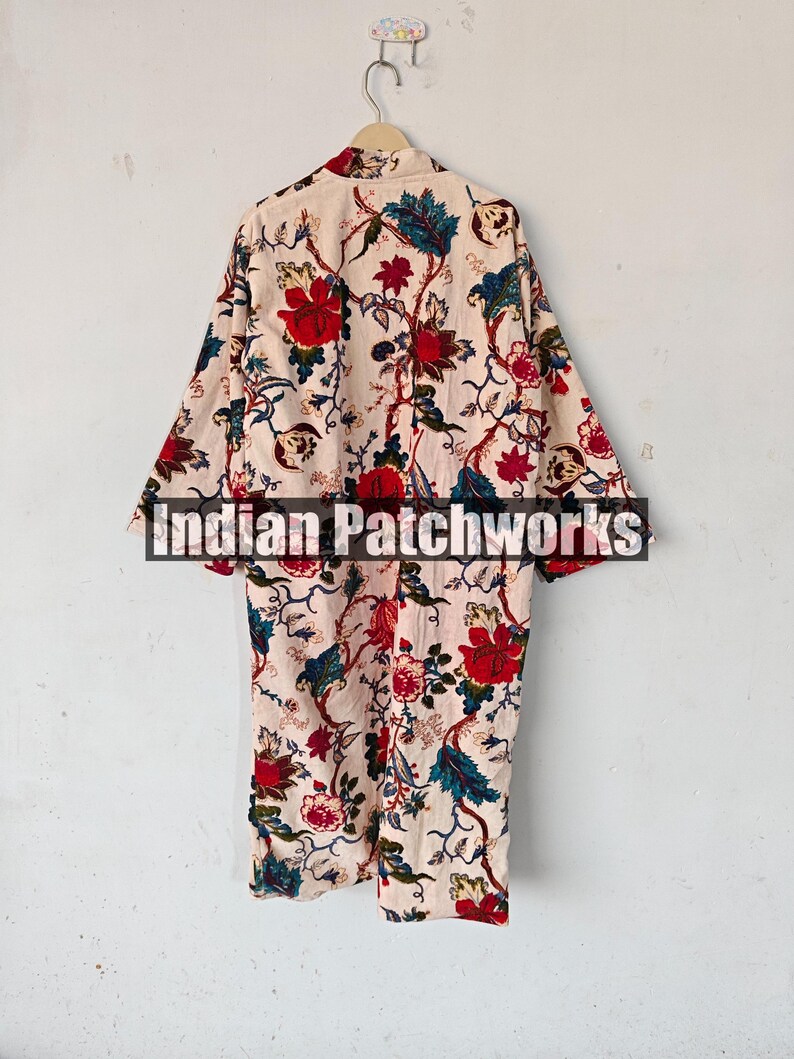 May include: A long-sleeved, cream-colored robe with a floral print featuring red, blue, and green flowers. The robe has a collar and a tie closure. The text "Indian Patchworks" is visible on the robe.