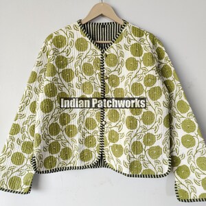 May include: A reversible quilted jacket featuring a white base with a green floral design. The jacket has a black and white striped lining and trim. It is buttoned and hangs on a wooden hanger.
