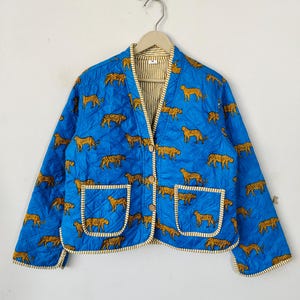 May include: A blue quilted jacket with a leopard print and a button closure. The jacket has two pockets and a white and yellow striped lining.
