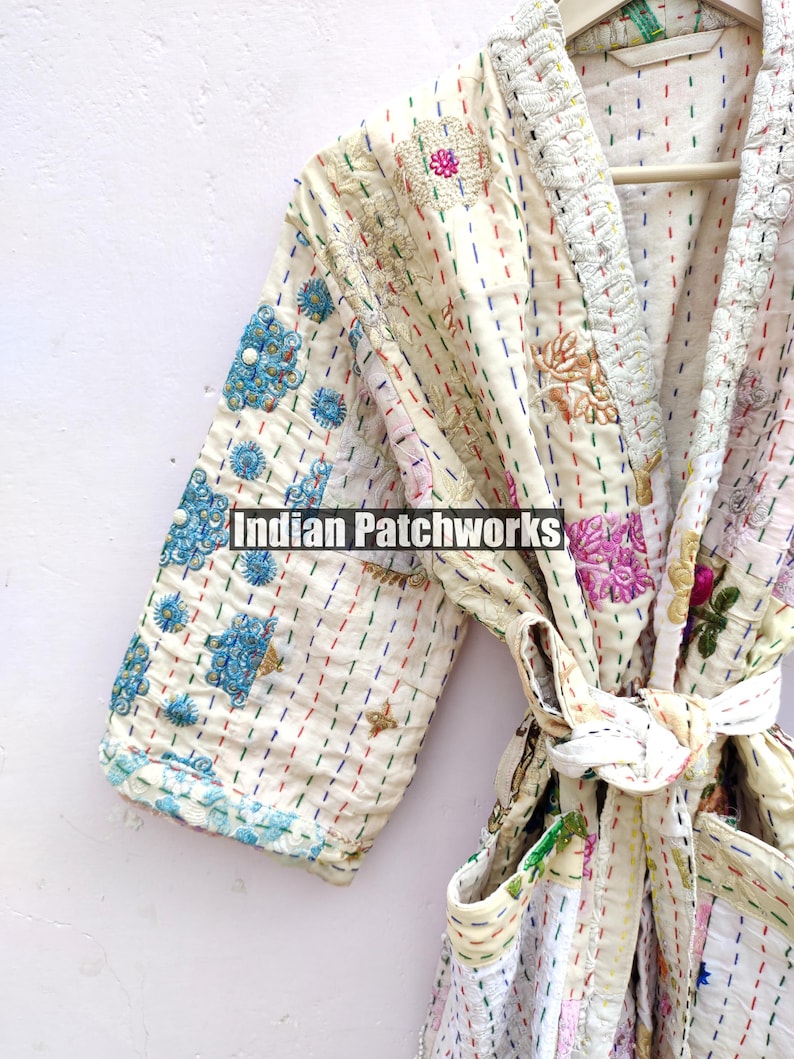 K&ouml;nnte beinhalten: Eine wei&szlig;e Baumwollrobe mit bunten Stickereien und einem Bindeg&uuml;rtel. Die Robe ist aus Patchwork-Stoff gefertigt und hat einen Vintage-Look.