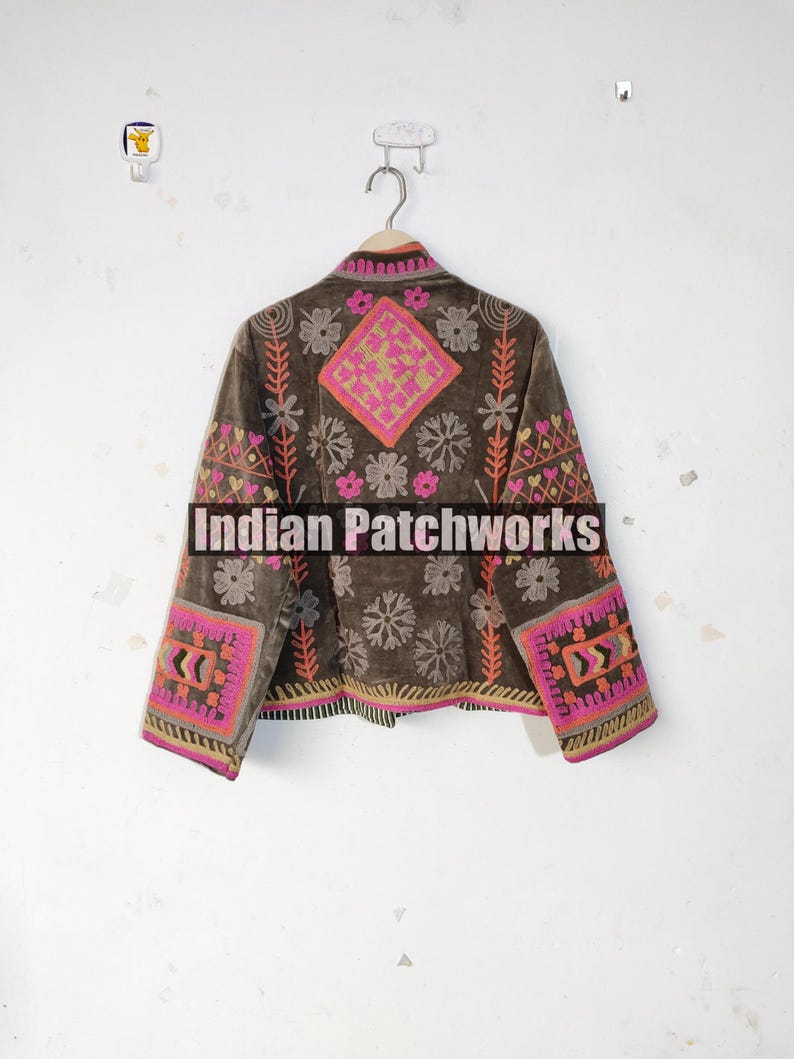 May include: A brown jacket with vibrant embroidery. The jacket displays pink, orange, and yellow floral and geometric patterns on the sleeves, back, and front. The text "Indian Patchworks" is across the front.
