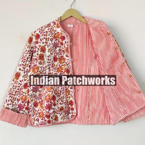 Op de afbeelding: Een omkeerbare jas met een bloemenprint aan de ene kant en rode en witte strepen aan de andere kant. De jas heeft een mandarijnsluiting en een knoopsluiting. De tekst "Indian Patchworks" is zichtbaar op de jas.
