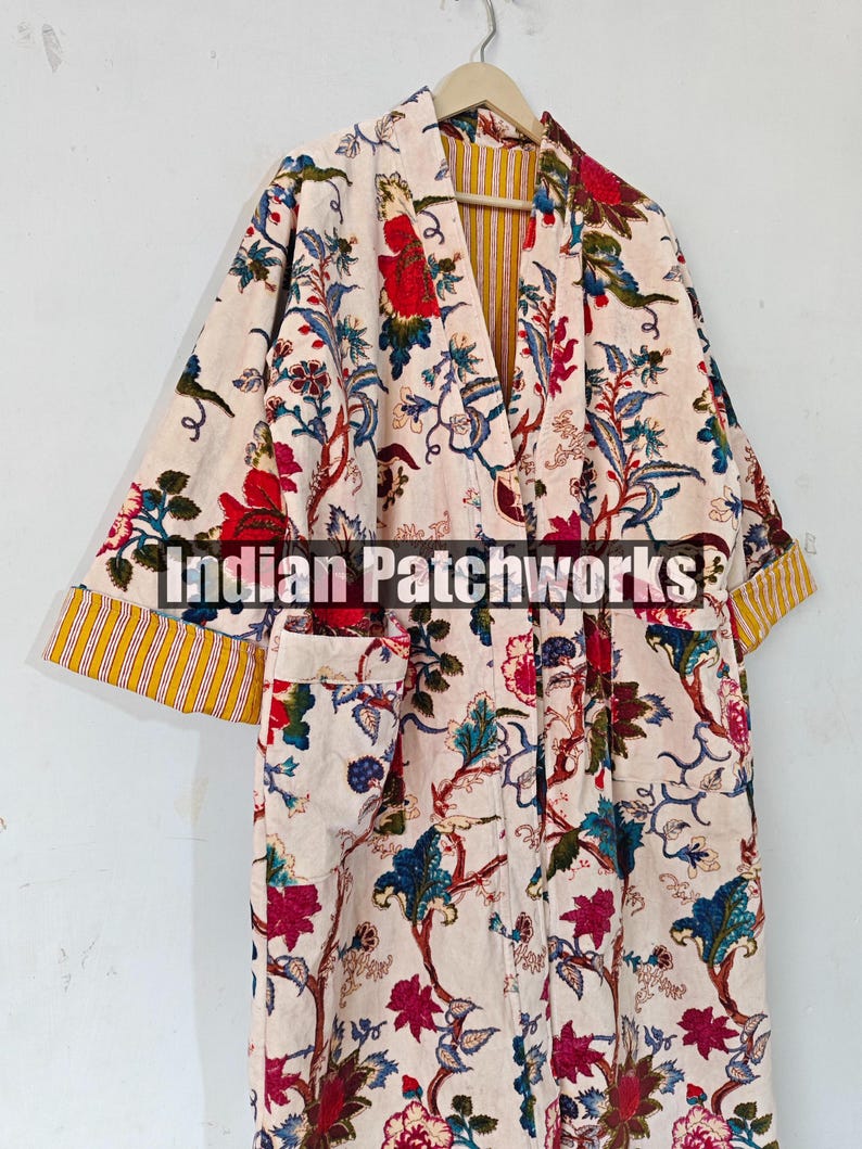 May include: A white cotton robe with a floral print in shades of red, blue, and green. The robe has a yellow and white striped lining and a yellow and red striped trim. The robe has a pocket on the left side.