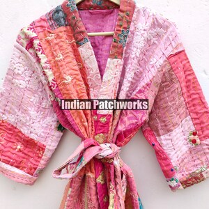 May include: A pink and peach patchwork kimono robe with a tie belt. The robe is made of quilted fabric and has a floral design. The text "Indian Patchworks" is printed on the robe.