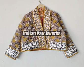 Puede incluir: Una chaqueta corta y entallada con estampado floral y un patrón de chevron en el ribete. La chaqueta está hecha de tela acolchada y tiene un ribete amarillo mostaza. El texto "Indian Patchworks" está impreso en la parte delantera de la chaqueta.