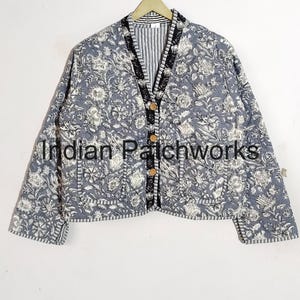 Könnte beinhalten: Eine graue gesteppte Jacke mit Blumendruck und schwarzem Besatz. Die Jacke hat einen Knopfverschluss und zwei Taschen. Der Text "Indian Patchworks" ist auf der Vorderseite der Jacke sichtbar.