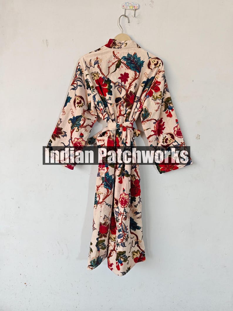 May include: A cream-colored robe with a floral print in shades of red, blue, and green. The robe has a long, flowing silhouette and a tie belt.