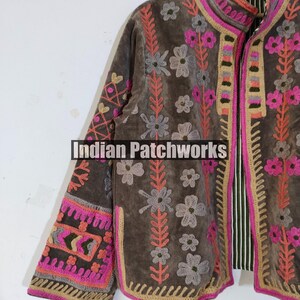 May include: A brown embroidered jacket with floral and geometric patterns. The jacket features pink, grey, and orange accents, with the text "Indian Patchworks" visible. The jacket has a striped lining and a high collar.