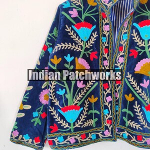 May include: A navy blue velvet jacket with colorful floral embroidery. The jacket has a mandarin collar and a front closure. The embroidery features a variety of flowers, leaves, and vines in shades of red, pink, blue, yellow, and green.