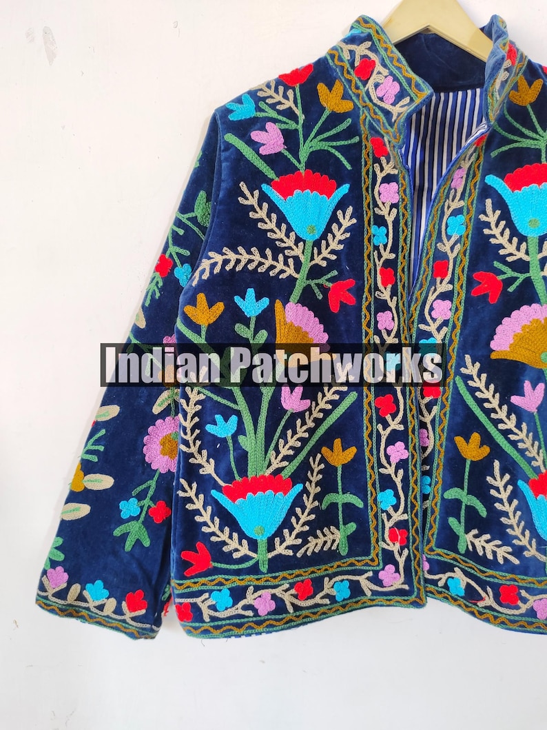 May include: A navy blue velvet jacket with colorful floral embroidery. The jacket has a mandarin collar and a front closure. The embroidery features a variety of flowers, leaves, and vines in shades of red, pink, blue, yellow, and green.