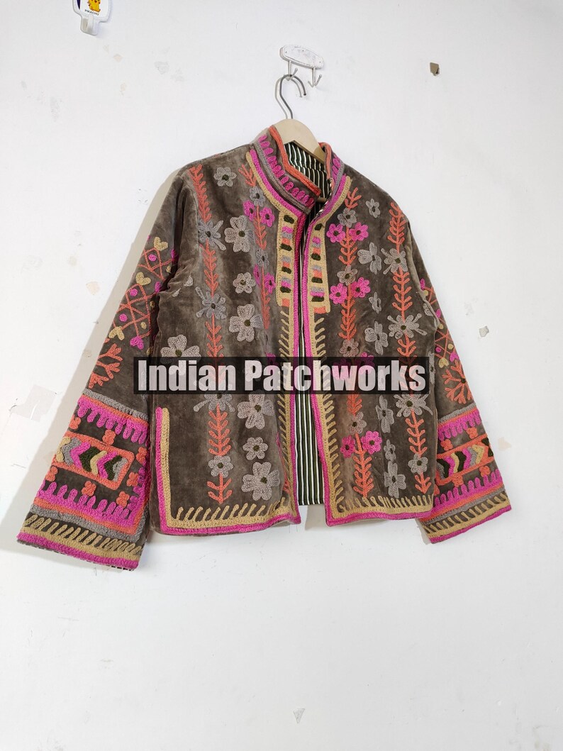 May include: A brown jacket with pink, orange, and grey floral embroidery. The jacket features a high collar and long sleeves with intricate patterns. The text "Indian Patchworks" is visible on the front.