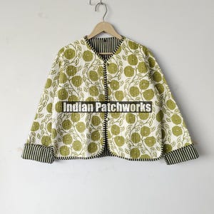 May include: A quilted jacket with a floral pattern in shades of green on a white background. The jacket has a round collar, long sleeves, and a striped trim. The text "Indian Patchworks" is visible.