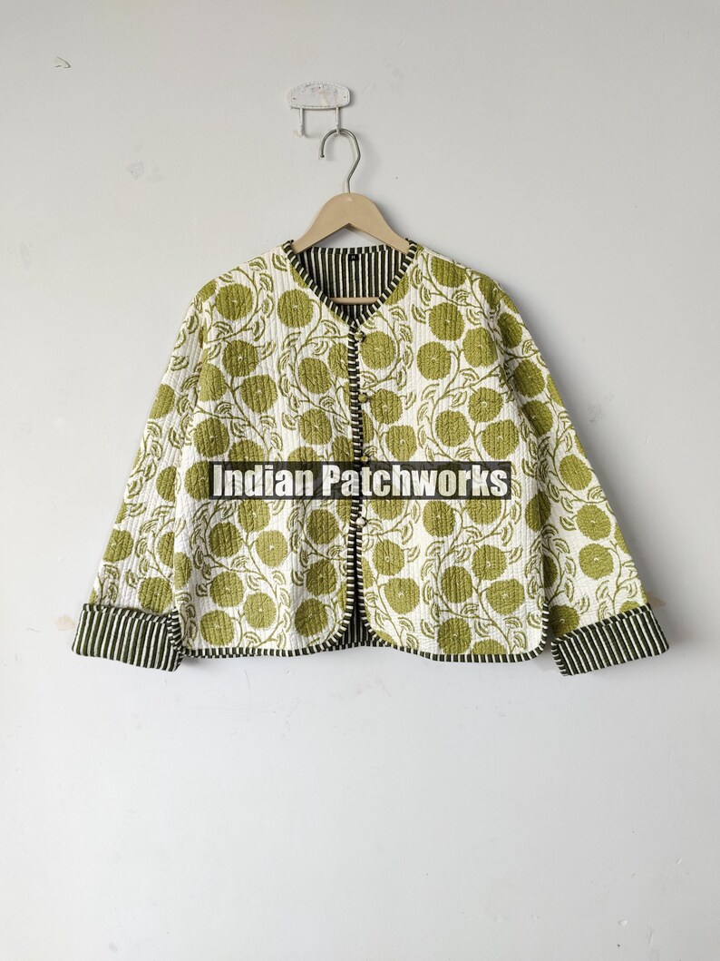 May include: A quilted jacket with a floral pattern in shades of green on a white background. The jacket has a round collar, long sleeves, and a striped trim. The text "Indian Patchworks" is visible.
