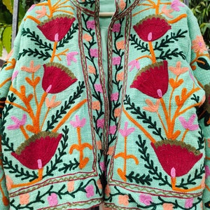 May include: A mint green embroidered jacket with a floral pattern. The jacket has a mandarin collar and a front zipper closure.