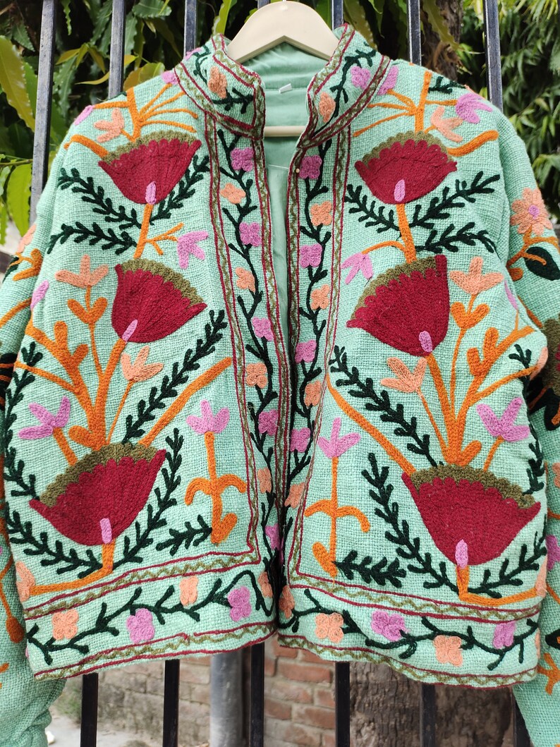 May include: A mint green embroidered jacket with a floral pattern. The jacket has a mandarin collar and a front zipper closure.