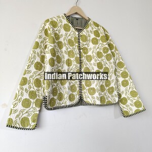 May include: A quilted jacket with a white background and a repeating pattern of green floral designs. The jacket has a black and white striped lining and trim. The jacket is hanging on a wooden hanger.