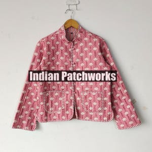 Könnte beinhalten: Gesteppte Jacke in Rosa mit weißem Blumenmuster. Die Jacke hat einen Stehkragen, zwei Vordertaschen und einen Knopfverschluss. Der Text "Indian Patchworks" ist auf der Vorderseite zu sehen.