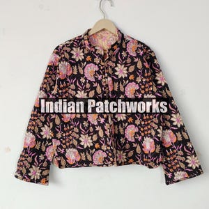 以下が含まれることがあります： ピンク、オレンジ、白の花柄の黒いジャケット。 ジャケットは長袖とマンダリンカラーです。 ジャケットの前面には「Indian Patchworks」の文字が表示されています。
