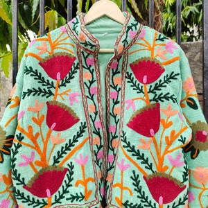 May include: A mint green embroidered jacket with a floral pattern in shades of red, orange, pink, and green. The jacket has a mandarin collar and a front zipper closure.
