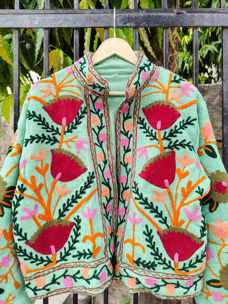 May include: A mint green embroidered jacket with a floral pattern in shades of red, orange, pink, and green. The jacket has a mandarin collar and a front zipper closure.