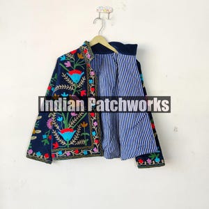 May include: A navy blue embroidered jacket with colorful floral patterns. The jacket has a striped lining and is hanging on a hanger.