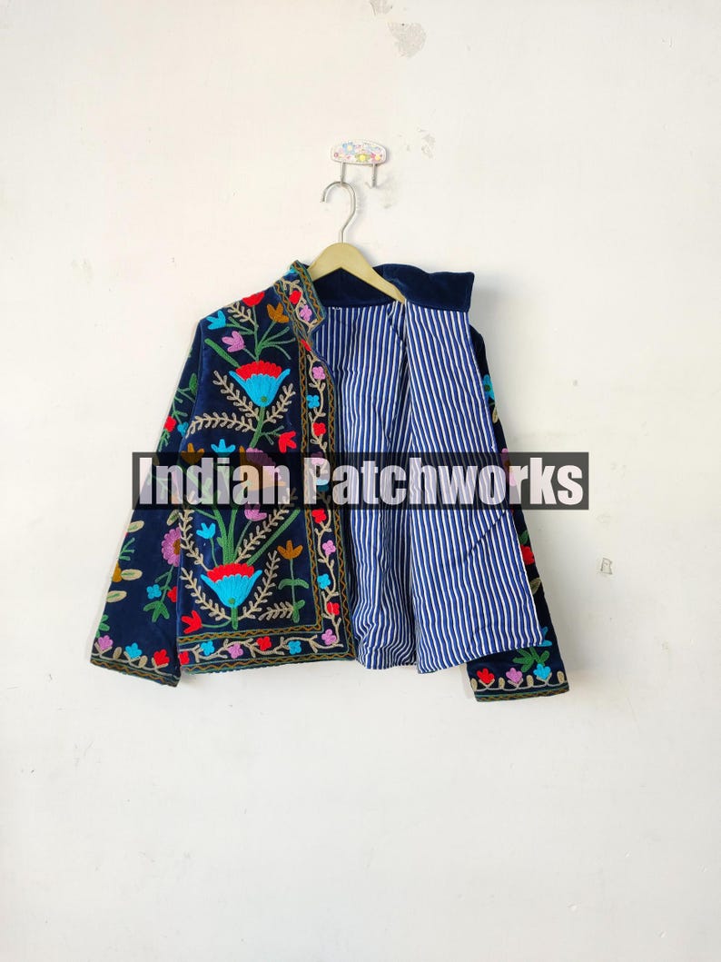 May include: A navy blue embroidered jacket with colorful floral patterns. The jacket has a striped lining and is hanging on a hanger.