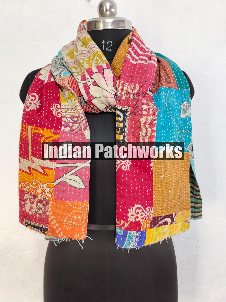 Puede incluir: Bufanda de patchwork colorida con el texto "Indian Patchworks" en la parte delantera. La bufanda presenta una variedad de telas en tonos de rosa, rojo, naranja, amarillo, azul y blanco. La bufanda est&aacute; colocada sobre un maniqu&iacute; negro.