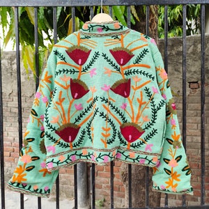 May include: A mint green embroidered jacket with floral patterns in shades of red, orange, green, and pink. The jacket has long sleeves and a cropped length.