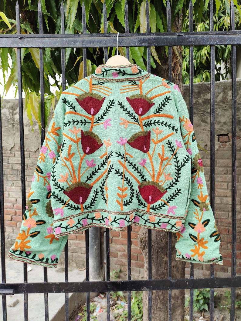 May include: A mint green embroidered jacket with floral patterns in shades of red, orange, green, and pink. The jacket has long sleeves and a cropped length.
