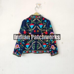 May include: A navy blue velvet jacket with colorful floral embroidery. The jacket has long sleeves and a mandarin collar. The text "Indian Patchworks" is visible on the jacket.