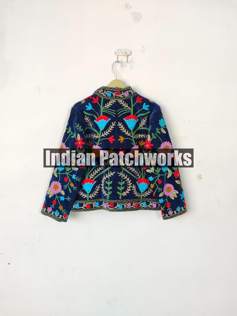 May include: A navy blue velvet jacket with colorful floral embroidery. The jacket has long sleeves and a mandarin collar. The text "Indian Patchworks" is visible on the jacket.