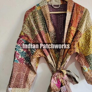 May include: A patchwork quilted robe with a tie belt. The robe is made of various fabrics in shades of brown, beige, pink, and green. The fabric is stitched together in a patchwork pattern. The robe has a long sleeve and a V-neck. The robe is hanging on a wooden hanger. The text "Indian Patchworks" is visible on the robe.